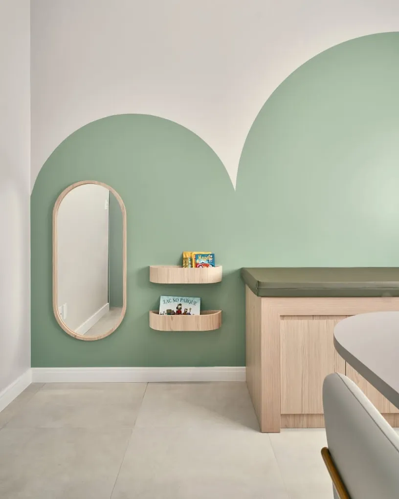 Sala de espera infantil da Clínica Majolí, com parede verde em formato de arco, espelho e prateleiras de livros